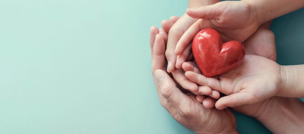 Un coeur rouge tenu par des mains d'enfant et ses parents adoptifs