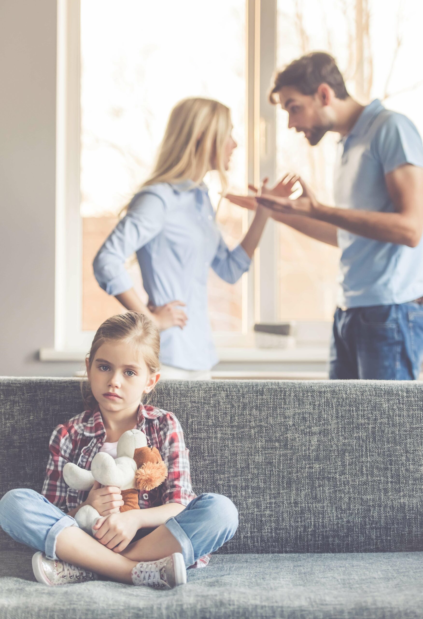 Enfant seule sur un canapé pendant que ses parents se disputent